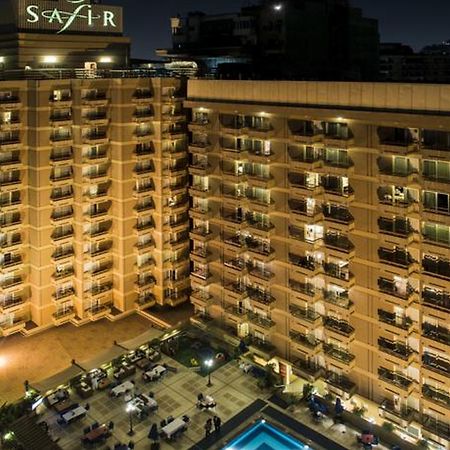 Safir Hotel Cairo Giza Exterior foto The photo shows a multi-story hotel building at night. The building is illuminated, showcasing multiple balconies along its facade. In front of the hotel, there is an outdoor area with seating arranged around a pool, which is also lit up. The hotel's