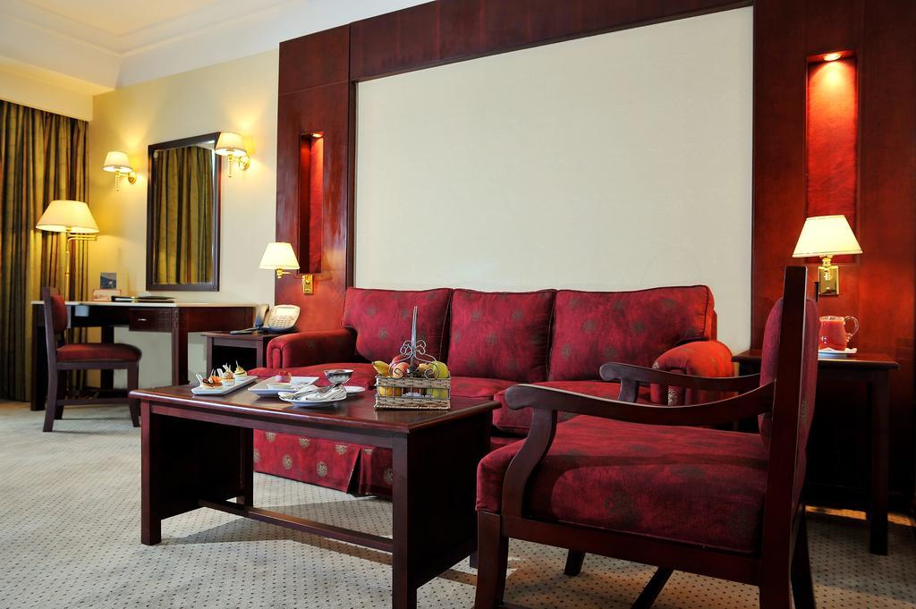 Safir Hotel Cairo Giza Quarto foto The photo shows a well-decorated hotel room or sitting area. In the center, there is a red couch with matching armchairs around it. A wooden coffee table is placed in front of the couch, and it holds some decorative items and snacks. The walls are ad